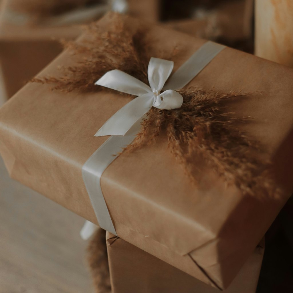 Prezent zapakowany w brązowy papier z białą wstążką i suszonymi trawami.